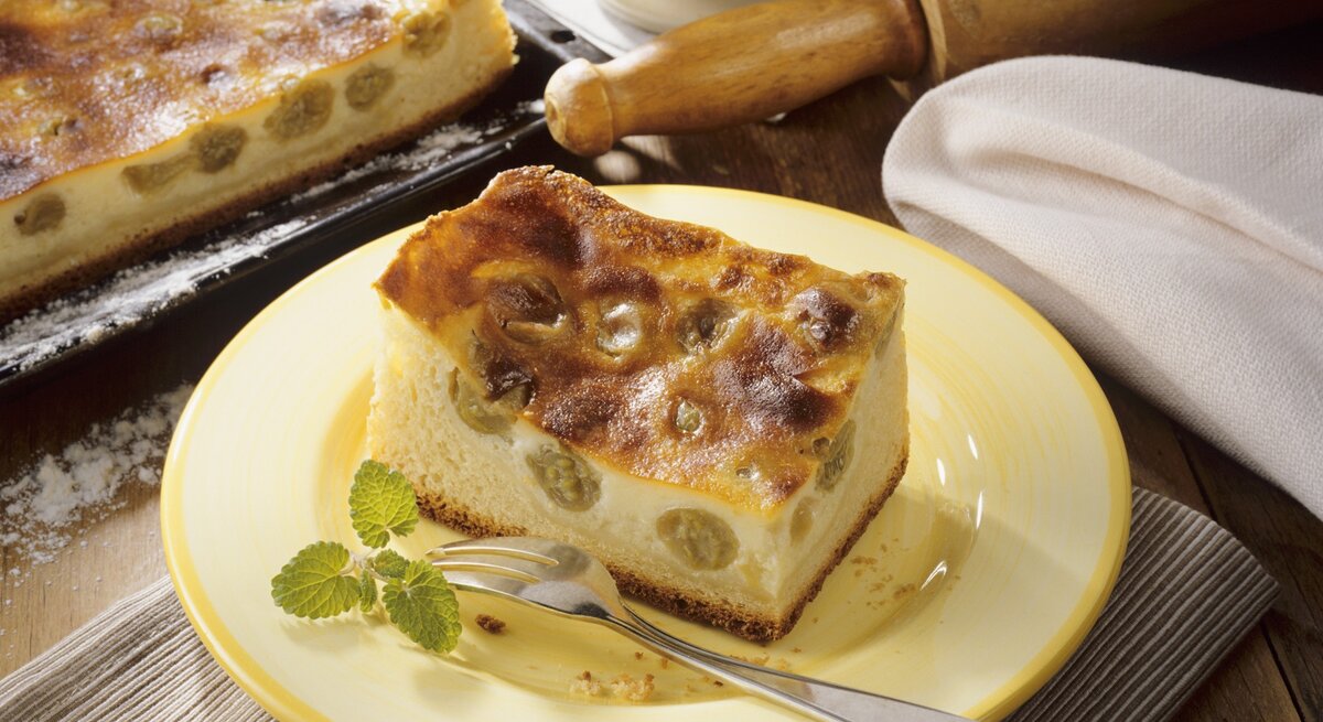Ein gelber Teller mit einem Stück Schmandkuchen auf einem rustikalen Holztisch von schräg oben fotografiert.