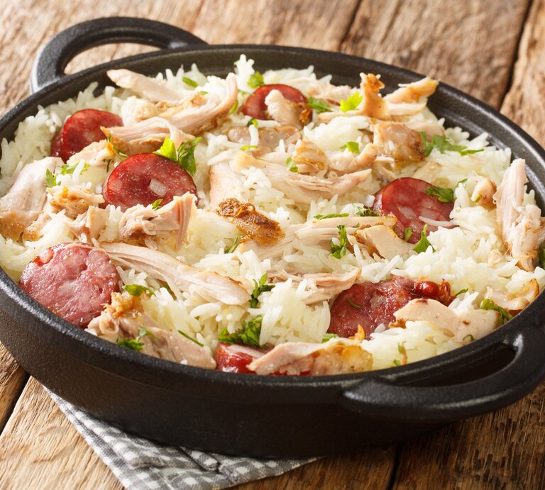One Pot Reis mit Huhn und gebratener Wurst in Gusspfanne auf Stoffserviette auf Holztisch. Aufnahme aus der Draufsicht. | © Getty Images / ALLEKO