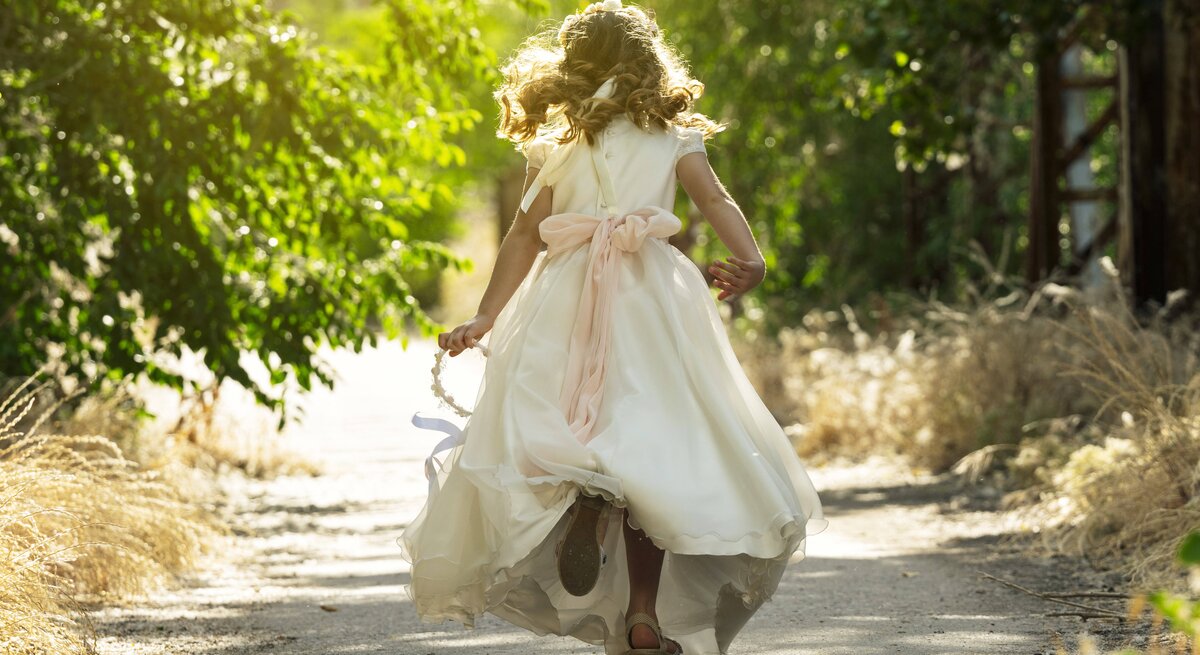 Ein Kind läuft in einem weißen Kleid einen Waldweg entlang