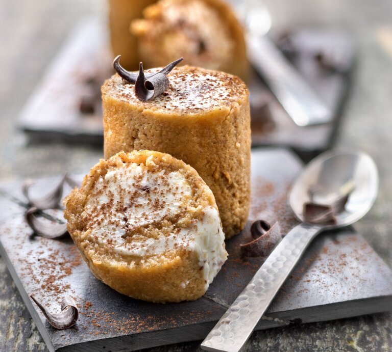 Tiramisu-Röllchen auf einem quadratischen schwarzen Brett. Daneben liegt ein Löffel.  | © StockFood / PhotoCuisine