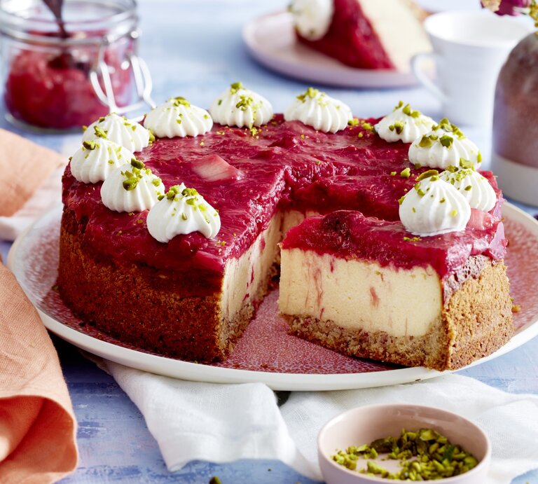 Auf einem Teller ist ein Rhabarber-Grieß-Cheesecake angerichtet. Er ist mit Sahnetüpfeln und Pistazien dekoriert. | © EAT CLUB / Isabell Triemer