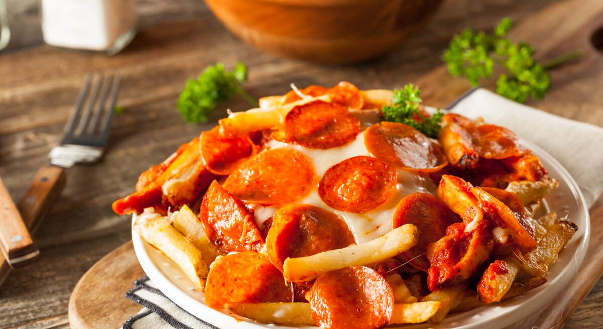 Pommes überbacken mit Salami auf hölzernem Untergrund. 