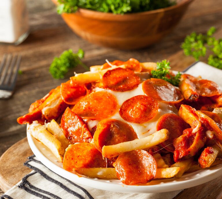 Pommes überbacken mit Salami auf hölzernem Untergrund.  | © Getty Images/bhofack2
