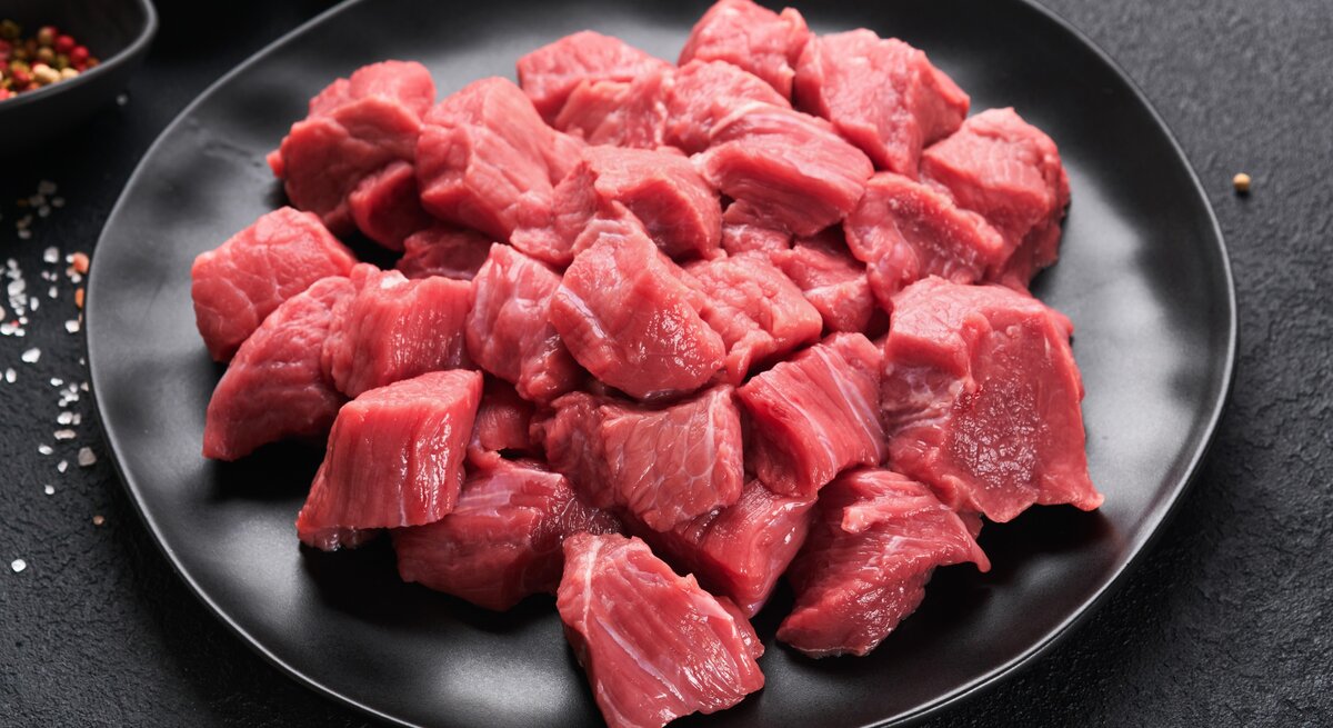 Ein schwarzer Teller mit dem Fleisch und einem grauen Hintergrund. Links neben dem Teller Gewürze und ein Bund Petersilie.