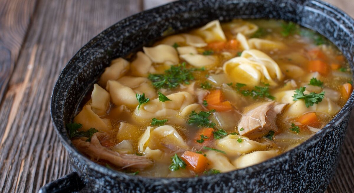 Ein Topf mit Tortellini-Hühnersuppe auf einem Holztisch.
