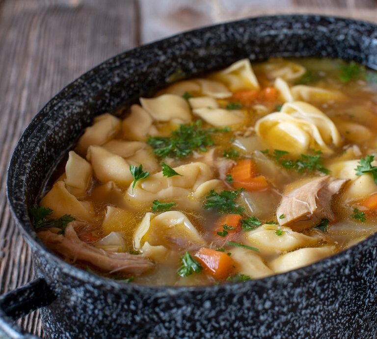 Ein Topf mit Tortellini-Hühnersuppe auf einem Holztisch. | © Shutterstock/Angelika Heine
