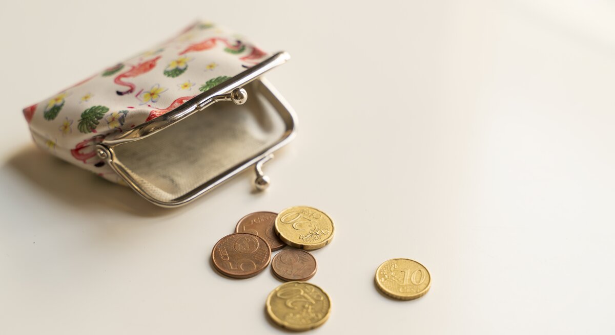 Eine leere Geldbörse und ein paar Cent-Stücke liegen auf einem weißen Untergrund.