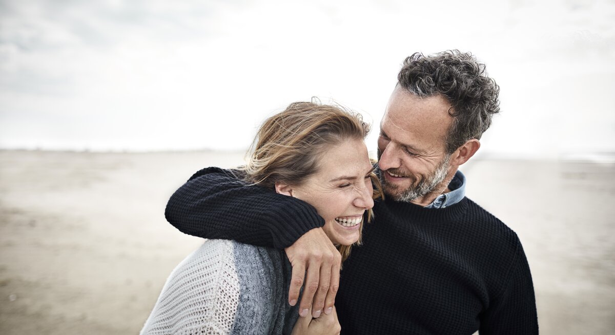 Zwei Menschen am Strand lachen miteinander. 