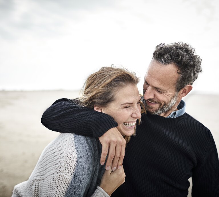 Zwei Menschen am Strand lachen miteinander.  | © GettyImages/Oliver Rossi