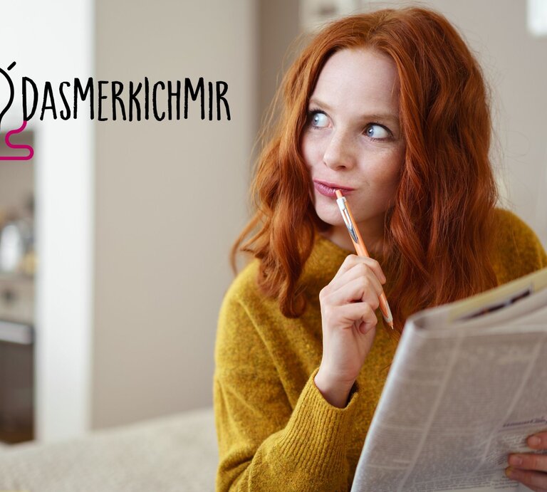Eine Frau mit rotem Haar und einem senfgelben Pullover liest nachdenklich eine Zeitung und hält dabei einen Stift an ihre Lippen. Ihr Blick ist nachdenklich und reflektierend, als würde sie über das Gelesene nachdenken oder eine Pause machen, um ihre Gedanken zu sammeln. Neben ihrem Kopf ist der Hashtag "#DAS MERK ICH MIR" neben einer stilisierten Glühbirnen-Grafik zu sehen, was darauf hindeutet, dass sie gerade eine Idee oder einen wichtigen Punkt zum Merken gefunden hat.  | © Shutterstock/stockfour