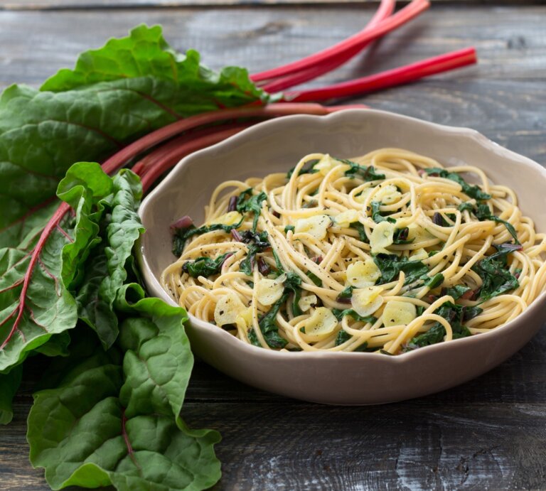 Pasta mit Mangold in cremiger Frischkäse-Soße in beigem Teller auf Holztisch. Daneben bunter Mangold. Draufsicht. | © Getty Images / OlgaLepeshkina