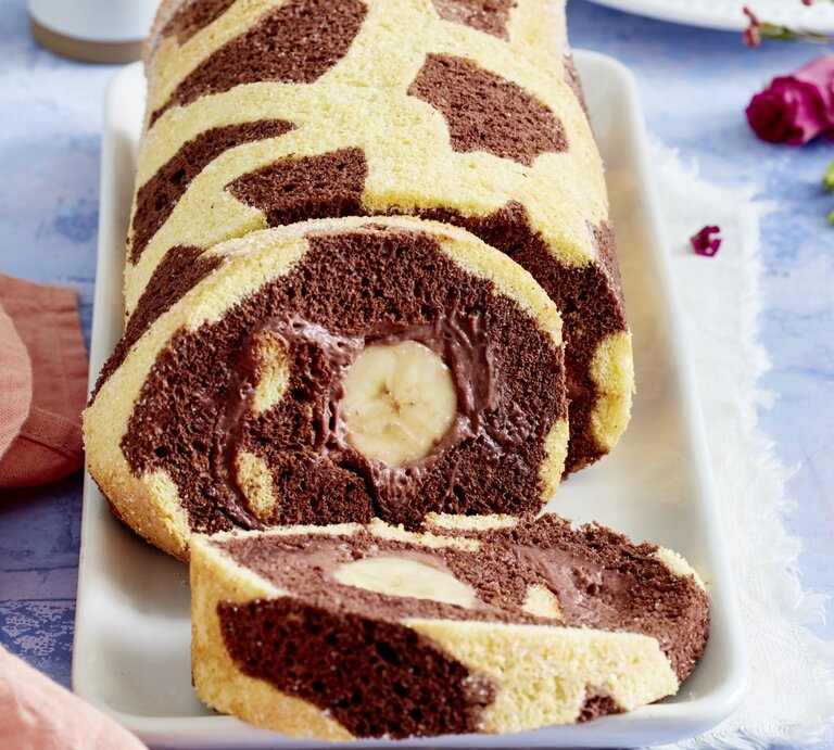 Angeschnittene Giraffen-Bananenrolle mit Schoko-Bananen-Füllung und dunklen Punkten auf hellem Teig. Untergrund hellblau.  | © EAT CLUB / Isabell Triemer