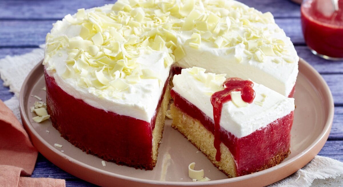 Frau-Holle-Kuchen mit Schneeflocken aus weißer Schokolade und Erdbeer-Glasur, angeschnitten serviert auf einem Kuchentablett auf blauem Holztisch. 