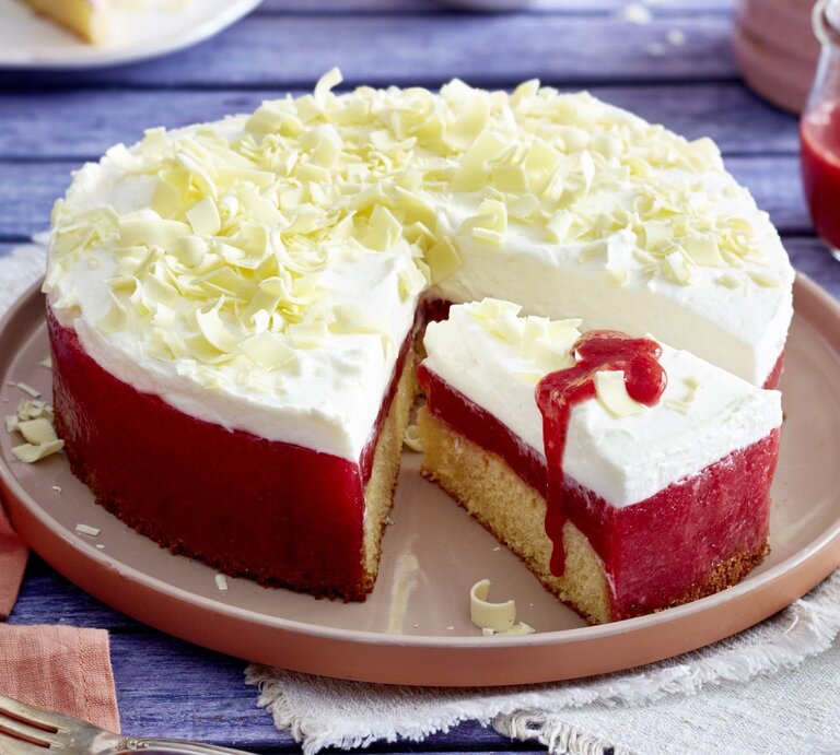 Frau-Holle-Kuchen mit Schneeflocken aus weißer Schokolade und Erdbeer-Glasur, angeschnitten serviert auf einem Kuchentablett auf blauem Holztisch.  | © Isabell Triemer