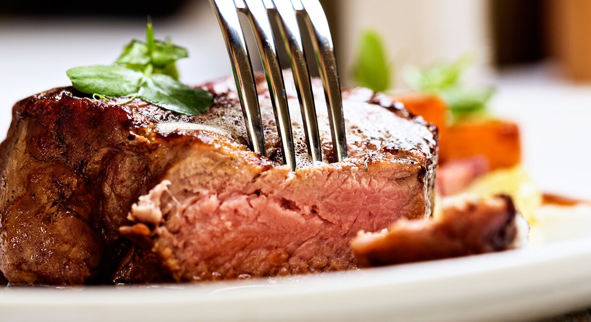 Gabel steckt in einem saftigen Stück Fleisch auf weißem Teller.