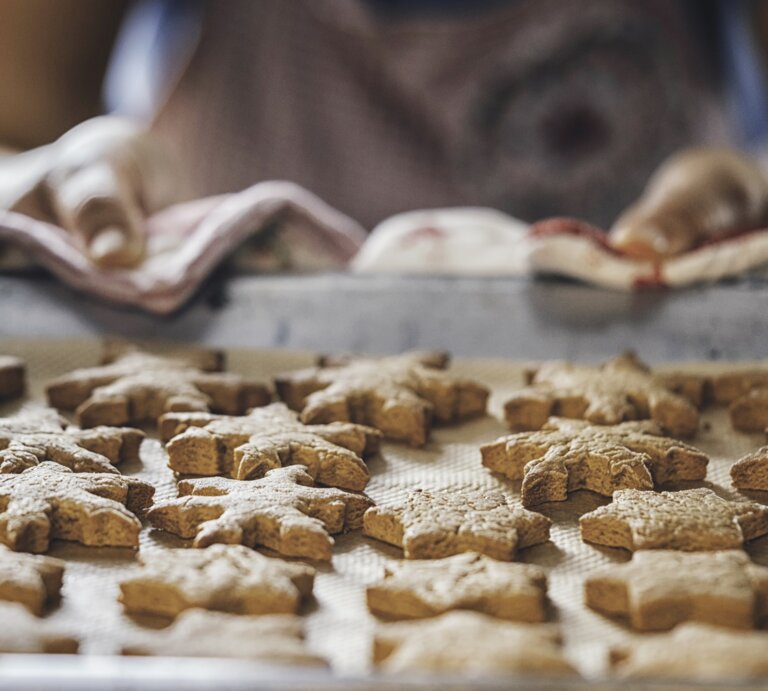 Frau zieht ein Backblech belegt mit sternförmigen Plätzchen aus einem Backofen.  | © iStock/GMVozd