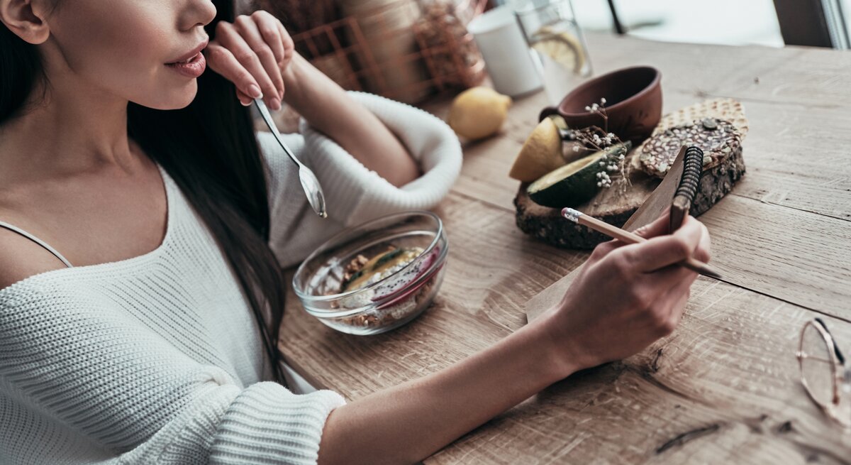 Frau sitzt an einem Holztisch und isst ein Müsli mit Flohsamenschalen. 