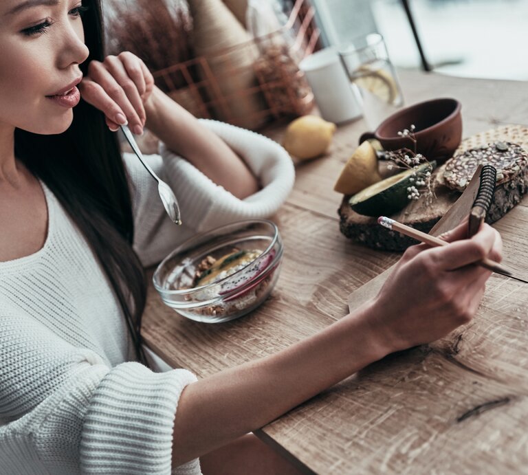 Frau sitzt an einem Holztisch und isst ein Müsli mit Flohsamenschalen.  | © iStock/G-Stock