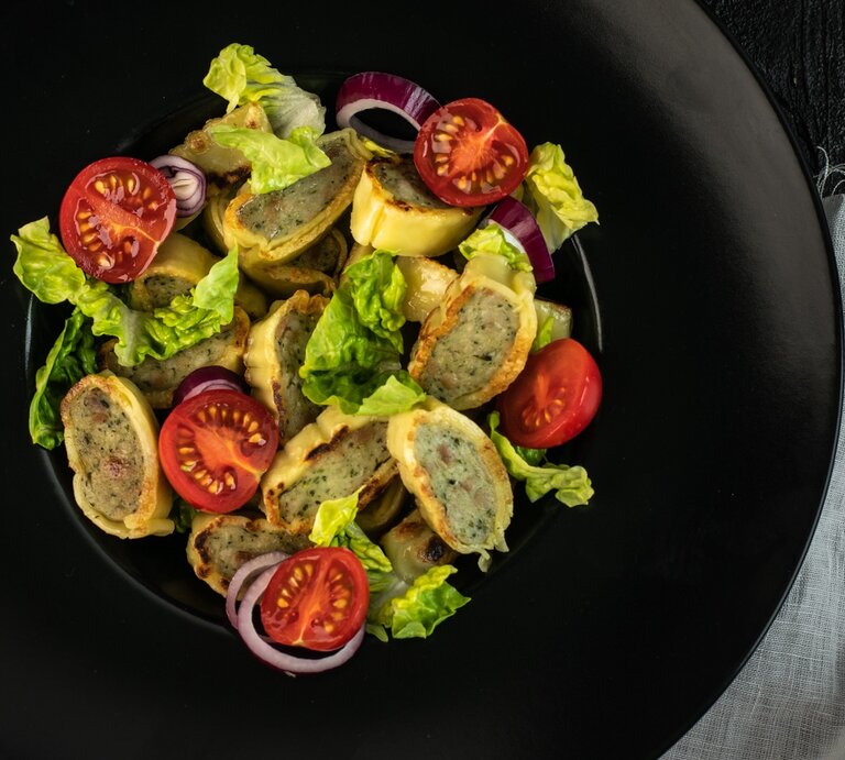 Ein schwarzer Teller mit dem Maultaschensalat auf einem dunklen Tisch mit hellgrauer Tischdecke. Direkt von oben fotografiert. | © Shutterstock/ Benita Kuszpit