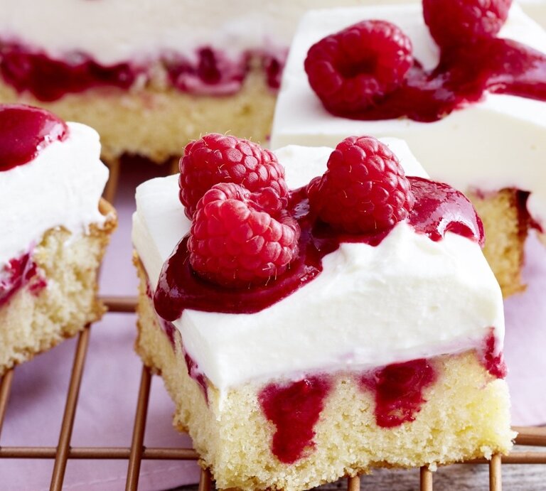 Himbeer-Mascarpone-Kuchen in eckiger Form, angeschnitten auf einem Kuchengitter auf rosanem Tischtuch. | © EAT CLUB / Isabell Triemer
