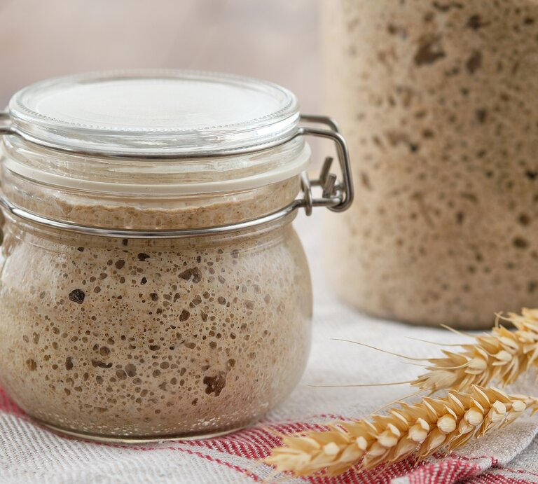 Frontal: Zwei Gläser mit einem großporigem Sauerteig auf einem Küchenhandtuch. So geht Sauerteig haltbar machen. | © Adobe Stock / Natallia