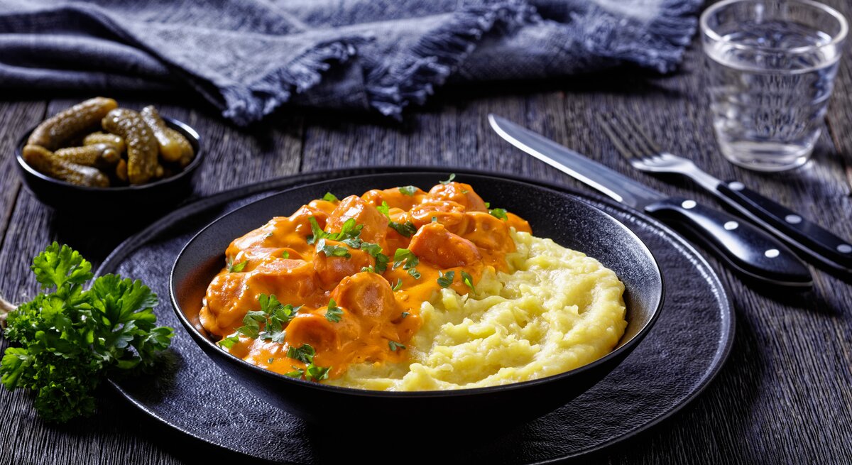 Finnischer Würstchen-Eintopf Nakkikastike mit Kartoffelpüree in schwarzer Schüssel.