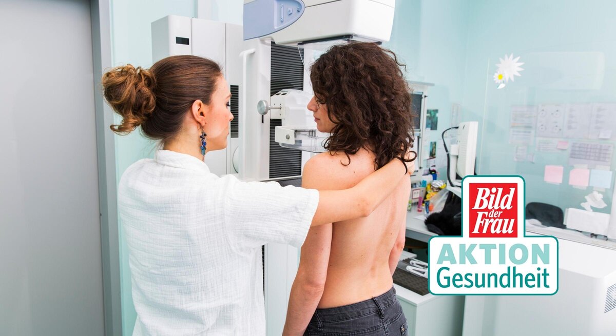 Eine medizinische Fachkraft in weißer Kleidung bereitet eine Mammographie-Untersuchung vor. Die Patientin steht ohne Oberbekleidung an dem Mammographie-Gerät und wird für die Aufnahme positioniert. Die Umgebung wirkt klinisch und professionell, mit einem hellen und sauberen Untersuchungsraum. Auf dem Bild ist auch das Logo von "Bild der Frau AKTION Gesundheit" zu sehen, was die Bedeutung von Vorsorgeuntersuchungen im Gesundheitsbewusstsein unterstreicht. Die Szene vermittelt einen wichtigen Aspekt der Frauengesundheit und präventiven Medizin.