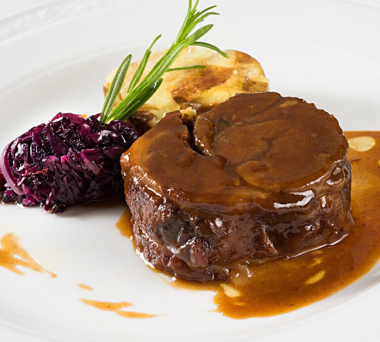 Glühweinbraten mit Soße übergossen, Rotkohl mit Rosmarinzweig und angebratener Knödel auf weißem Teller aus der Draufsicht. | © Getty Images / Burcu Atalay Tankut