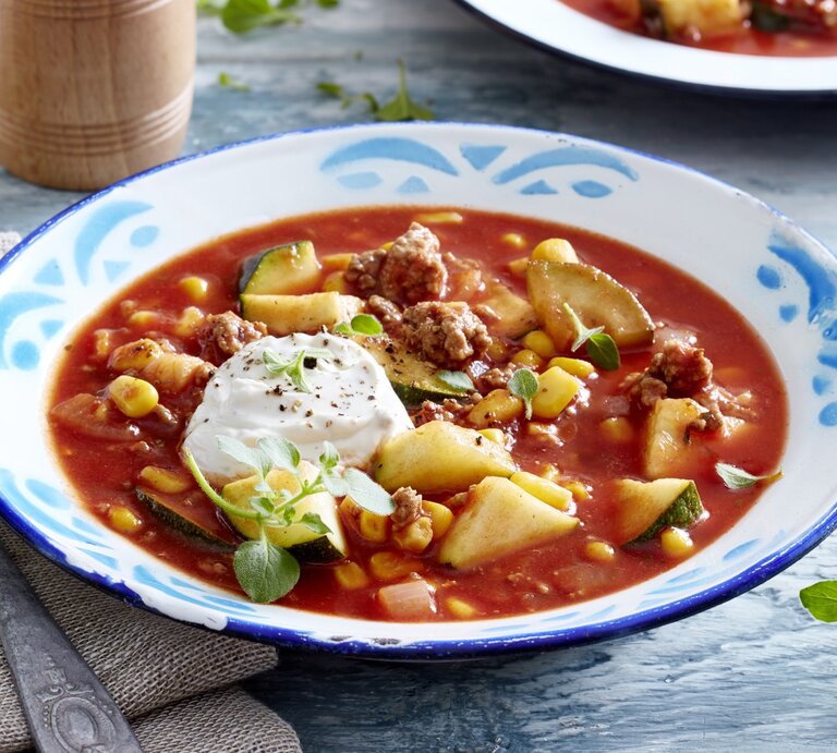 Auf einem tiefen Teller ist eine Portion Zucchini-Tomaten-Eintopf mit Hack serviert. Sie wird mit Frischkäse verfeinert. | © EAT CLUB / Isabell Triemer