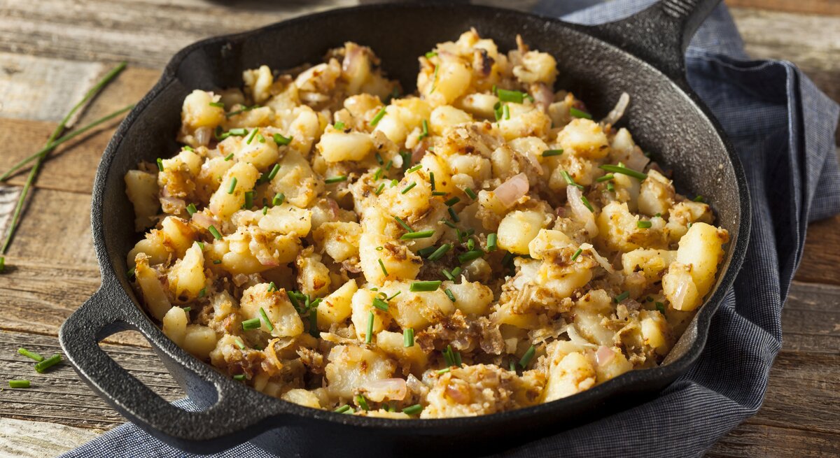 Gebratene Kartoffelstreusel in gusseiserner Pfanne auf hölzernem Untergrund.