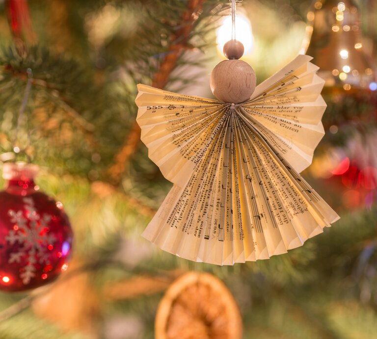 Selbst gebastelter Engel aus Notenblättern hängt am Weihnachtsbaum. | © Adobe Stock/hk13114