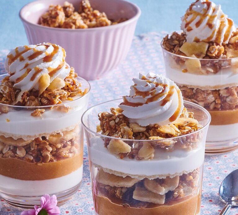 Auf einem Tisch stehen vier Gläser geschichtetes Apfel-Karamell-Parfait. Sie sind mit Sahne und Karamellsoße überzogen.  | © StockFood / Profimedia