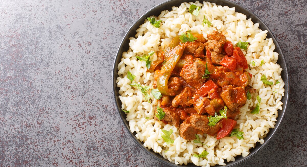 Draufsicht: Runde Schüssel / gekochte Nudeln und Gulasch. Es handelt sich um den ungarischen Rindfleisch-Eintopf Pörkölt.