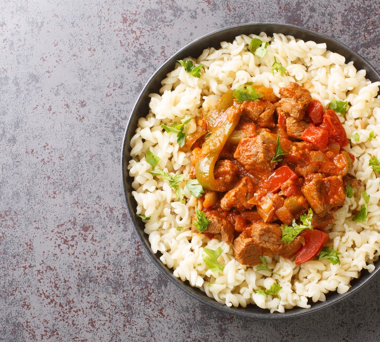 Draufsicht: Runde Schüssel / gekochte Nudeln und Gulasch. Es handelt sich um den ungarischen Rindfleisch-Eintopf Pörkölt. | © Getty Images / ALLEKO