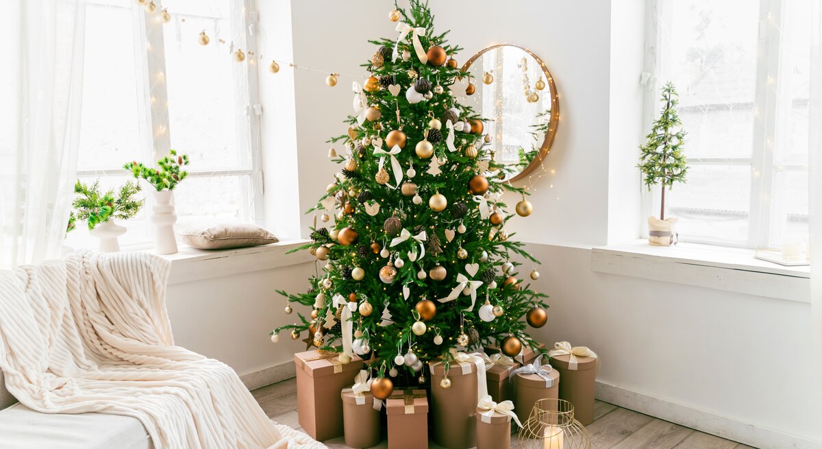 Weihnachtsbaum mit goldenen Kugeln steht im Wohnzimmer. Auch die andere Weihnachtsdeko ist in Gold gehalten. 