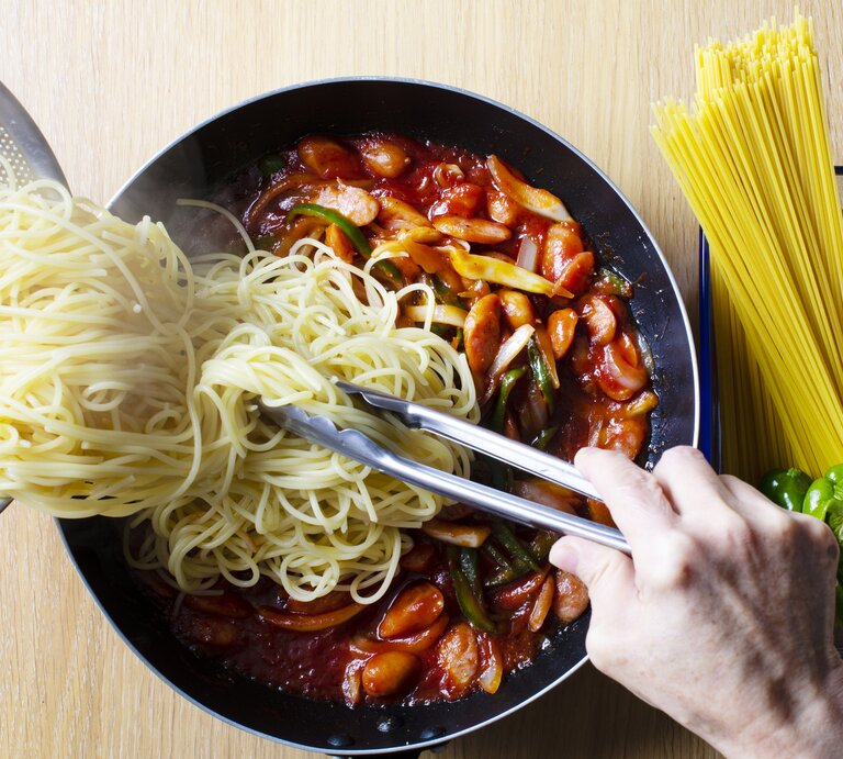 Spaghetti werden aus einem Sieb in eine tomatige Gemüsesoße gekippt. | © Getty Images/ Yuuji