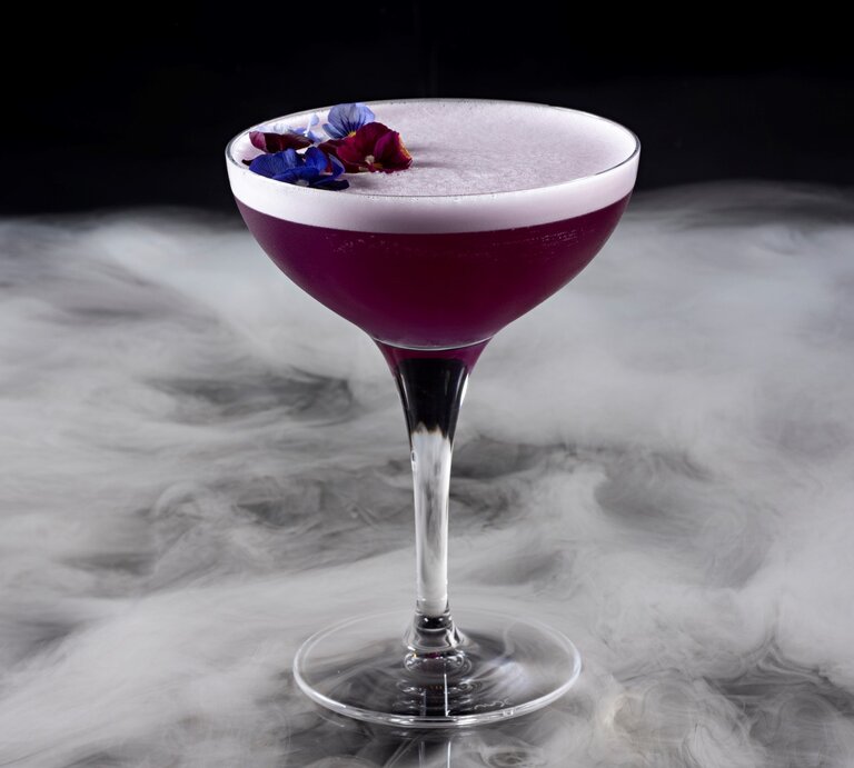 Ein Stielglas mit dem violetten Cocktail auf einem nebelartig-marmoriertem Untergrund. | © Gettyimages/ BURCU ATALAY TANKUT