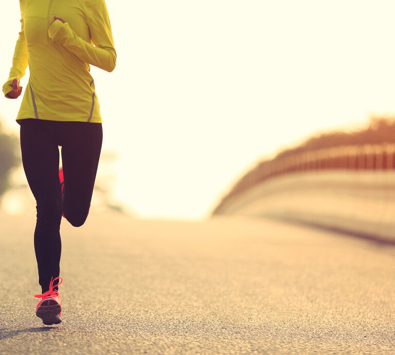  Ein Läufer in auffälliger Sportbekleidung joggt auf einer Straße, umgeben von sanftem Sonnenlicht und einer ruhigen Landschaft, was auf Training bei Tagesanbruch oder Sonnenuntergang hindeutet. | © iStock.com/Li Zhongfei