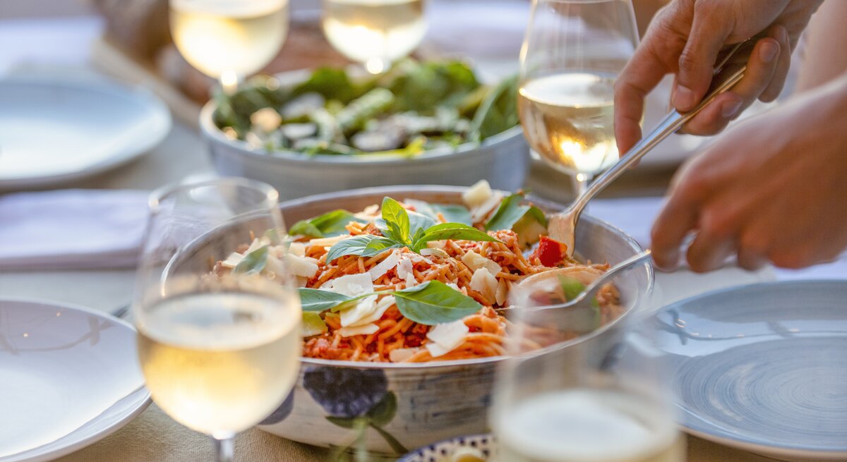 Silberfarbene Schüssel gefüllt mit Spaghett-Salat umrundet von Weingläsern.