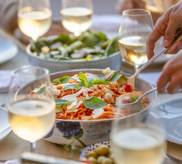 Silberfarbene Schüssel gefüllt mit Spaghett-Salat umrundet von Weingläsern. | © Getty Images/courtneyk