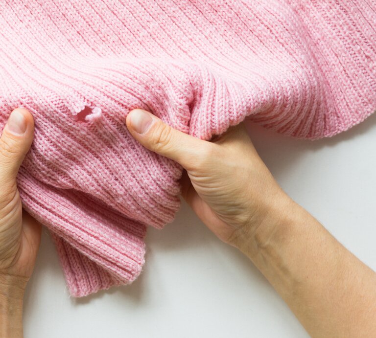 Ein rosa Pullover hat ein kleines Loch. | © iStock / na Gorbunova