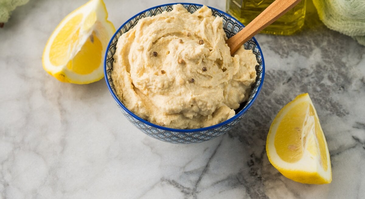 Schüssel / Zitrus-Hummus / Zitronenspalten / Marmortisch / Nahaufnahme / Draufsicht, schräg