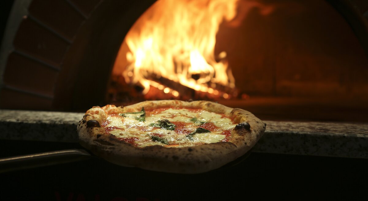 Eine Pizza wird in den heißen Ofen geschoben. 