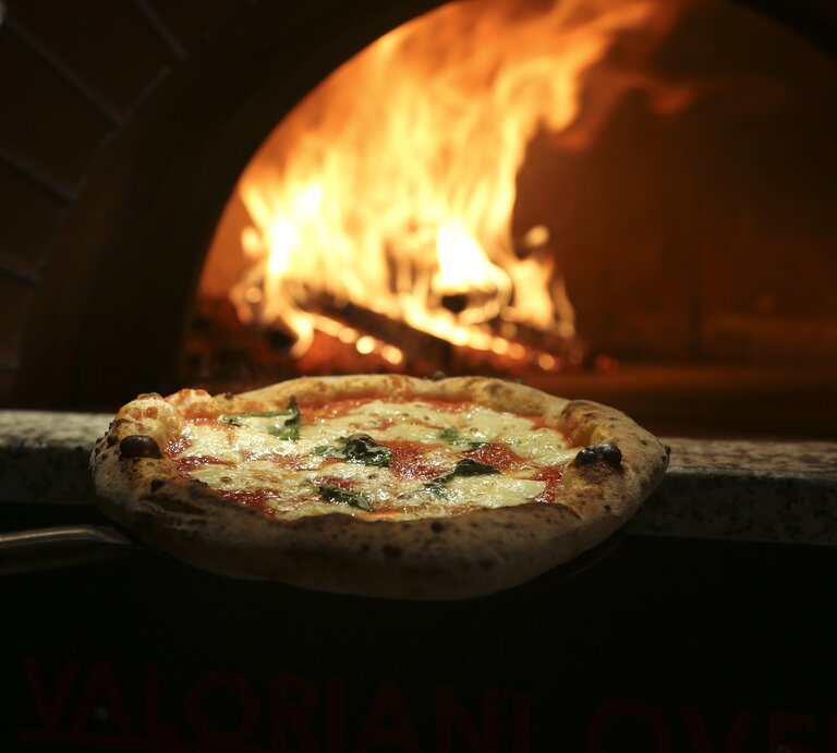 Eine Pizza wird in den heißen Ofen geschoben.  | © iStock.com/Mariha-kitchen