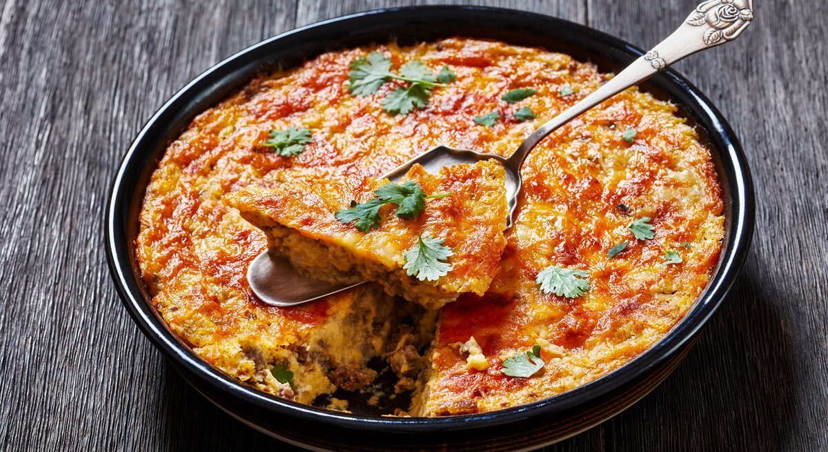 Hackfleisch-Grieß-Auflauf in dunkler, runder Auflaufform auf dunklem Holz. 