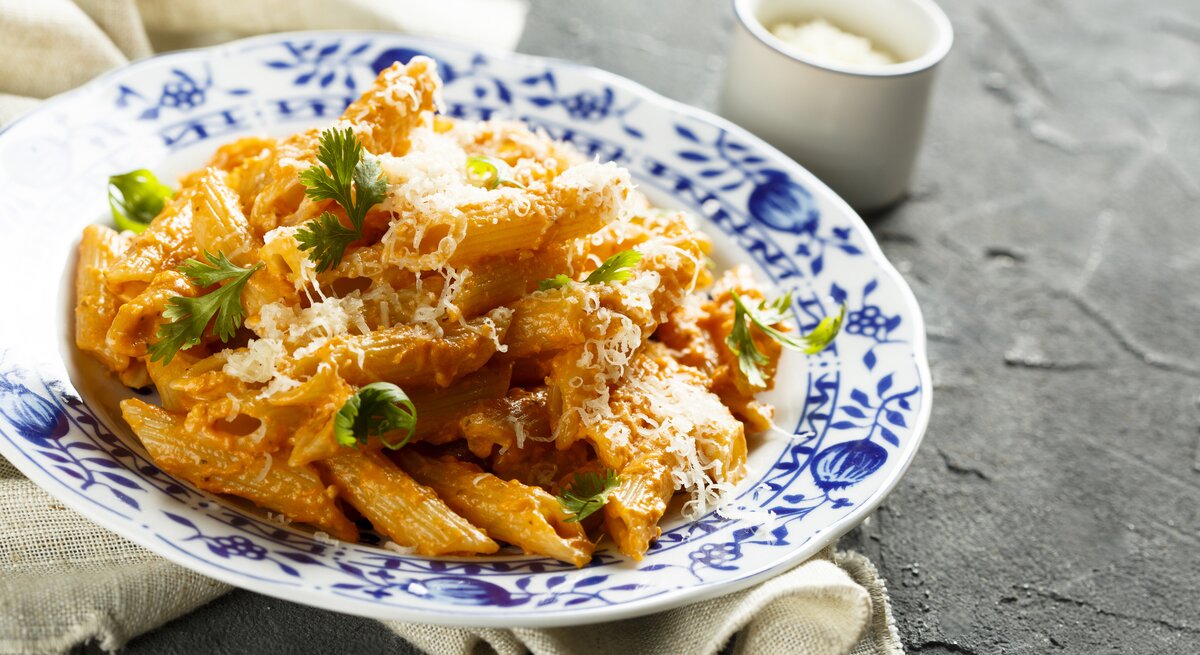Altmodischer Teller belegt mit penne in Paprika-Sahne-Soße – bestreut mit geriebenem Parmesan und Petersilie. 