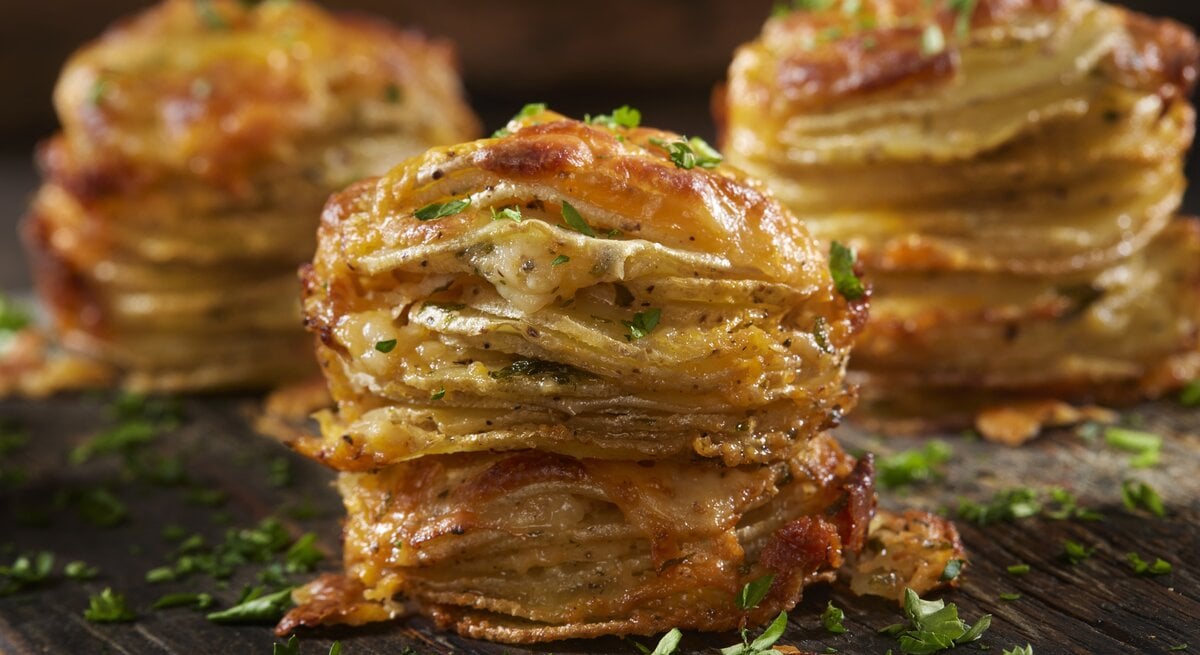 Käsige Kartoffelstapel mit Petersilie bestreut auf einem Holzbrett. 