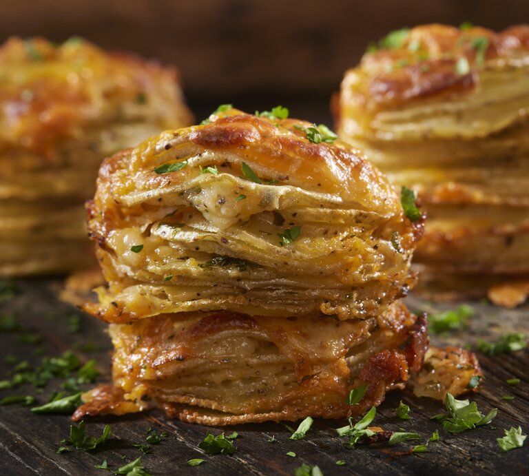 Käsige Kartoffelstapel mit Petersilie bestreut auf einem Holzbrett.  | © Getty Images/LauriPatterson