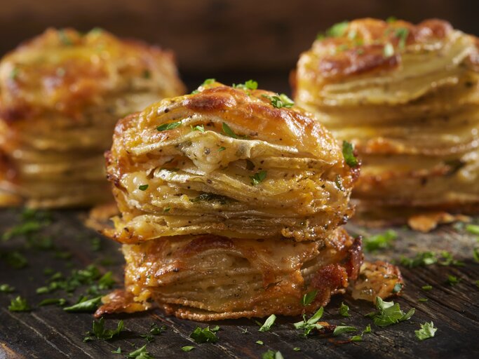 Käsige Kartoffelstapel mit Petersilie bestreut auf einem Holzbrett.  | © Getty Images/LauriPatterson