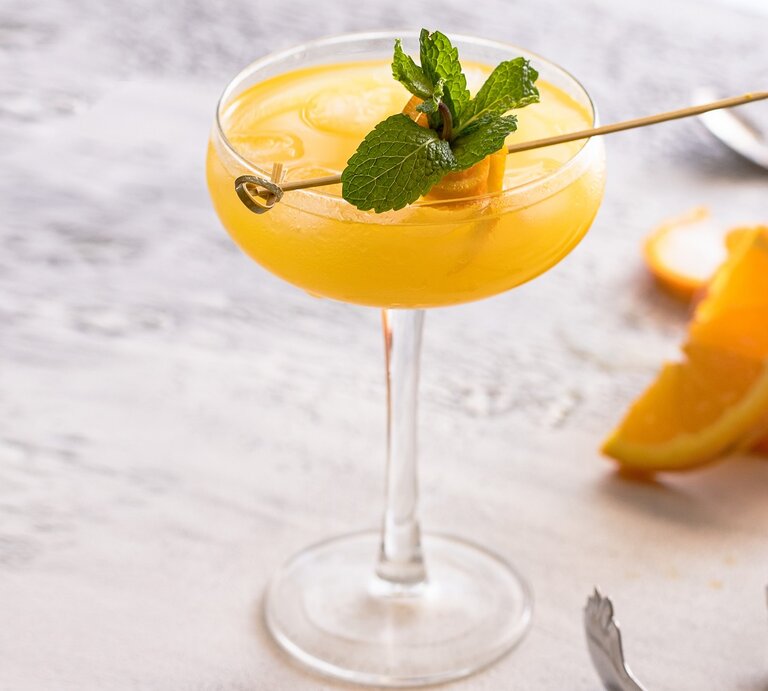 Ein Coupette-Glas mit dem gelben Drink auf einem grauen Holztisch. | © Shutterstock/ vasanty